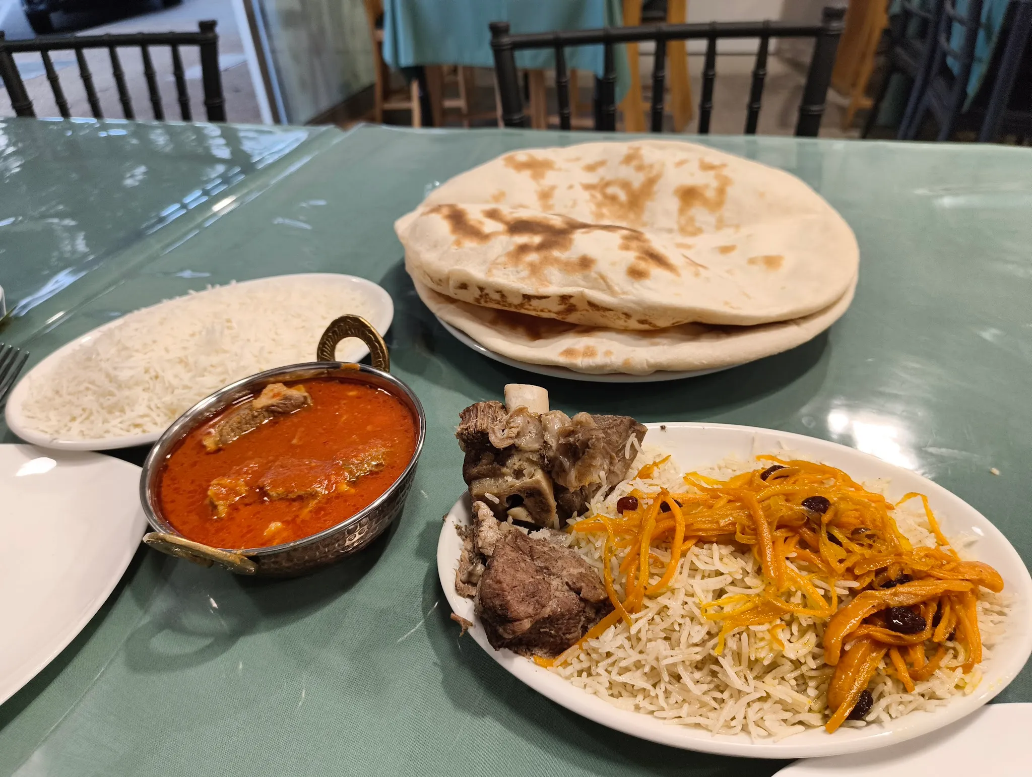 Afghan food spread on a teal table: kabuli pulao rice, karahi curry in a brass pot, and stacked naan bread