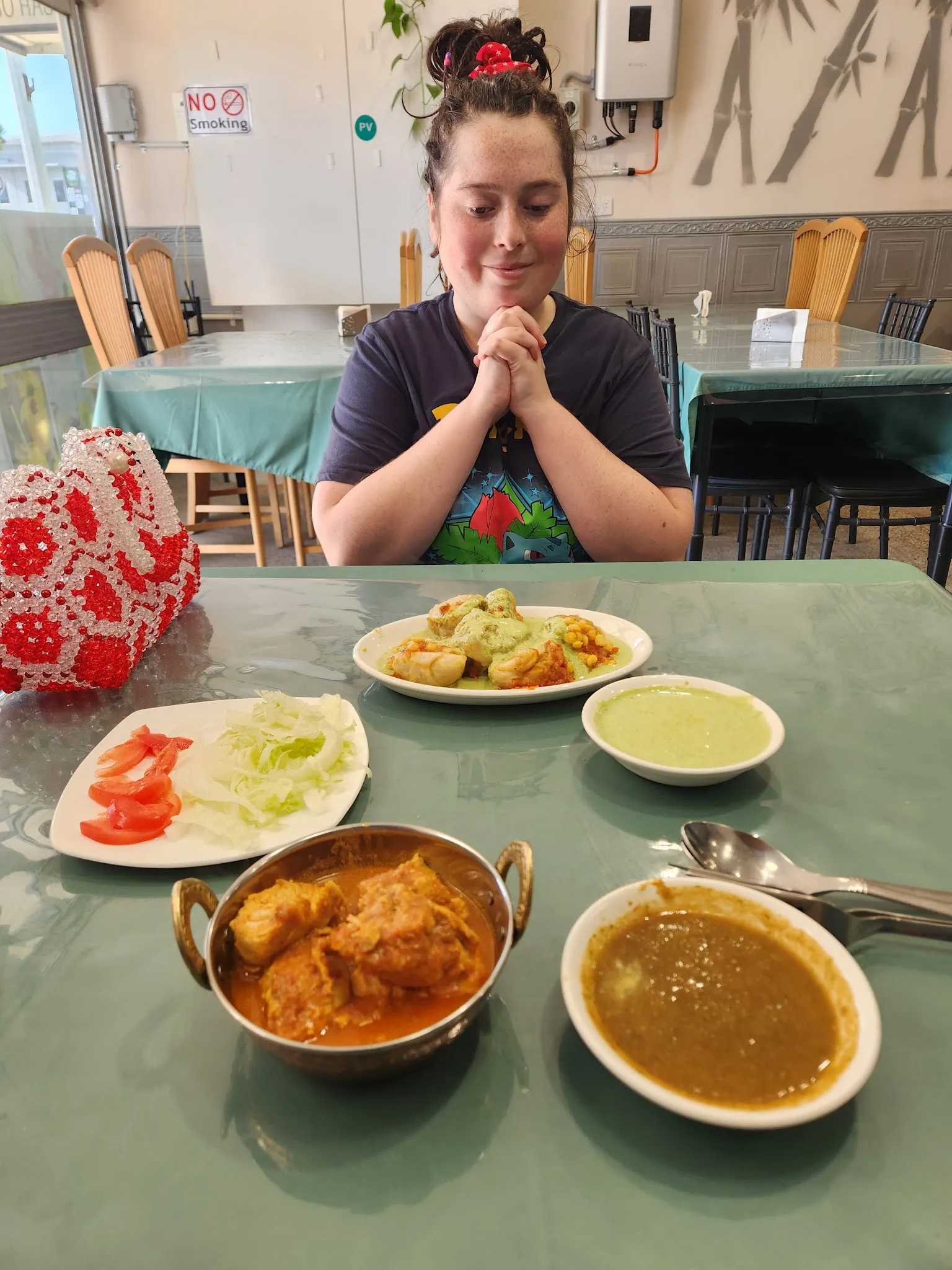 Customer smiling at a table with multiple Afghan dishes including karahi curry and daal, bamboo mural on wall behind